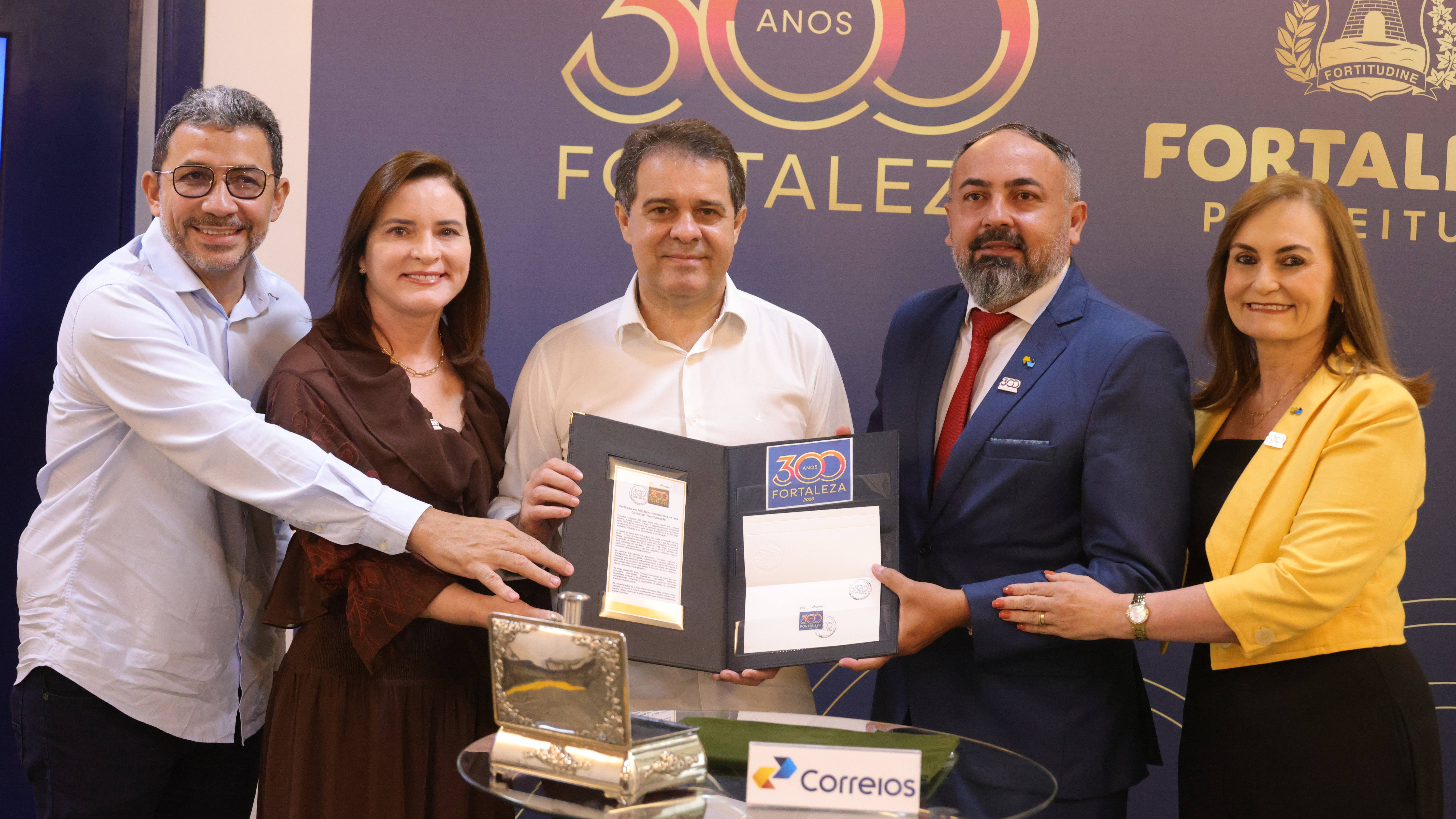 O prefeito Evandro Leitão, a primeira-dama Cristiane Leitão e representantes dos Correios posam para foto mostrando o selo comemorativo dos 300 anos de Fortaleza